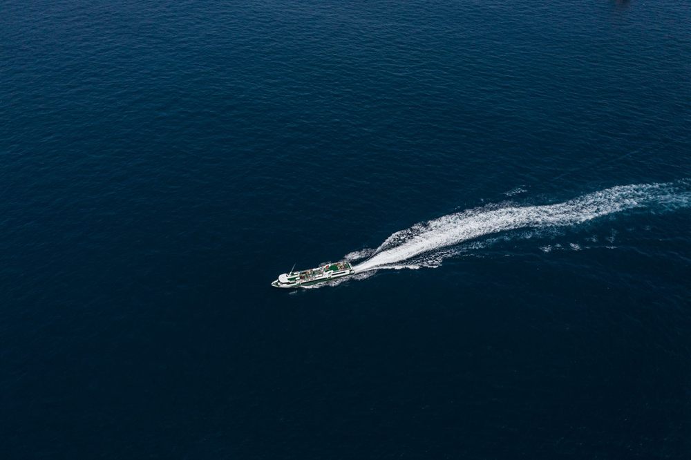 Aerial view of a ship leaving a long wake across a deep blue ocean